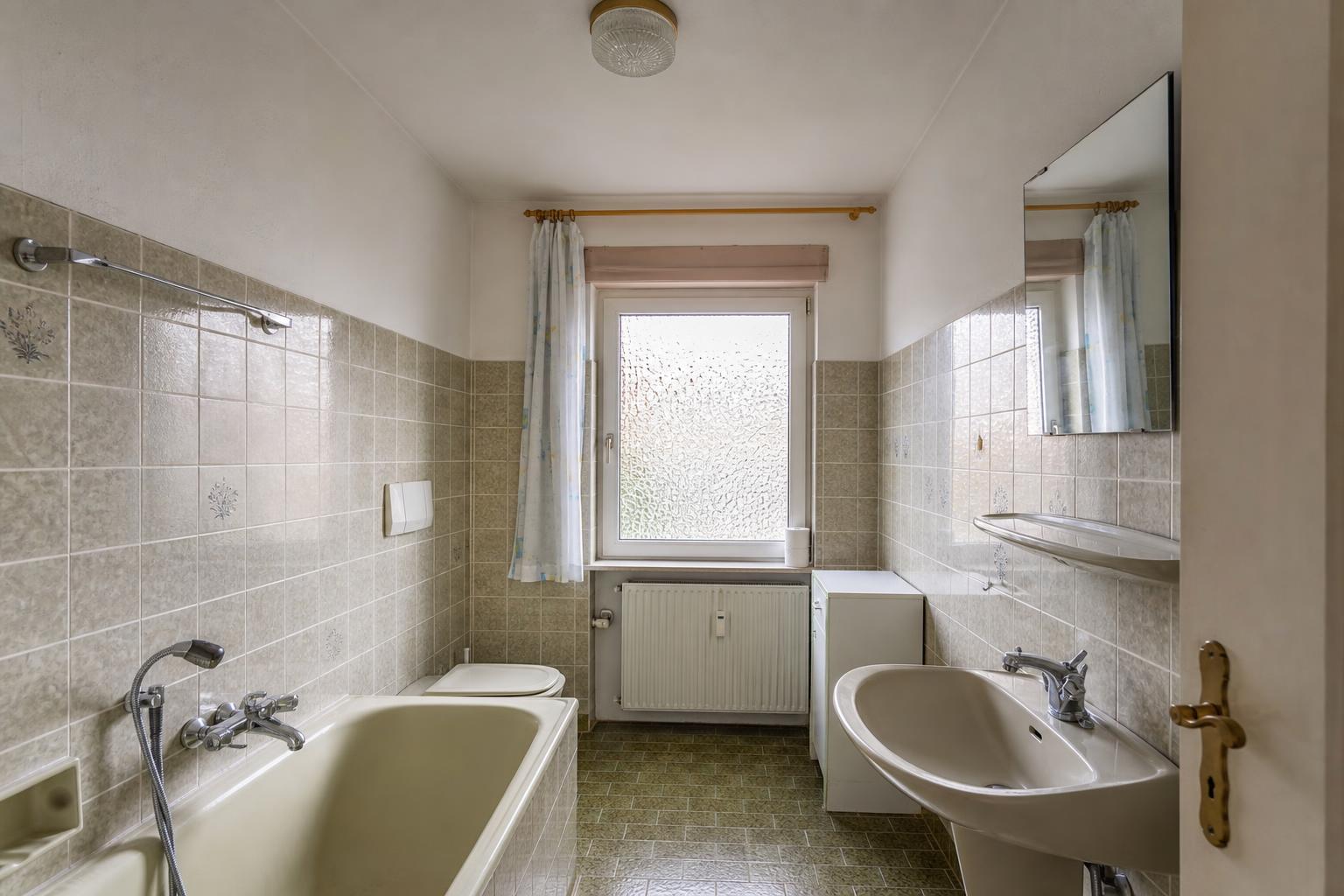 Älteres Badezimmer mit gefliesten Wänden und älterer Sanitärausstattung.